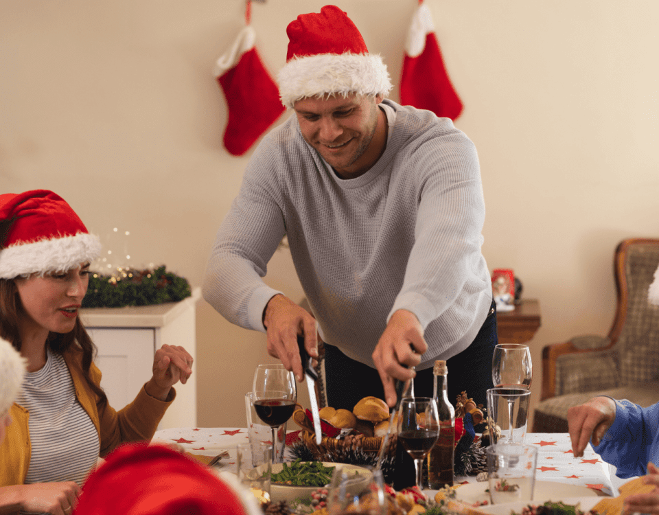 Family having a healthy Christmas dinner. All members are wearing Santa hats, and a man is standing and serving food.