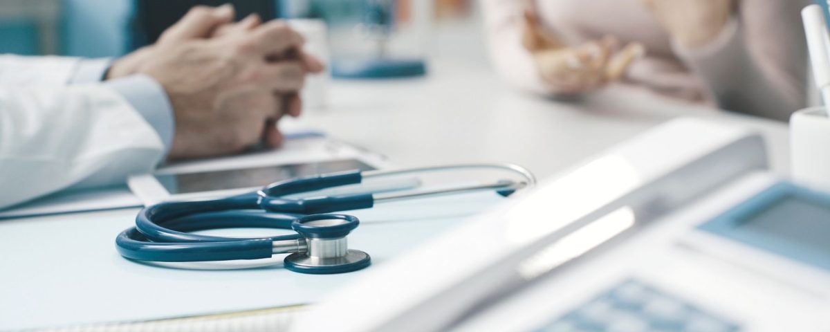 Desk with stethoscope in focus and bariatric surgeon's and patient's hands in background