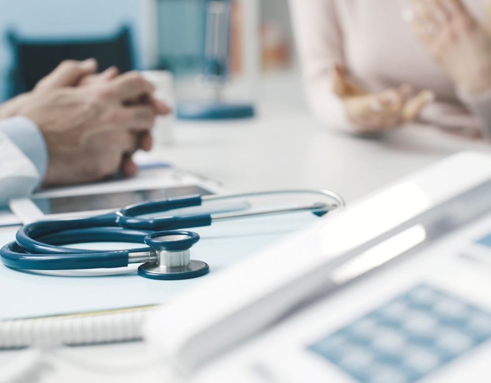 Desk with stethoscope in focus and bariatric surgeon's and patient's hands in background